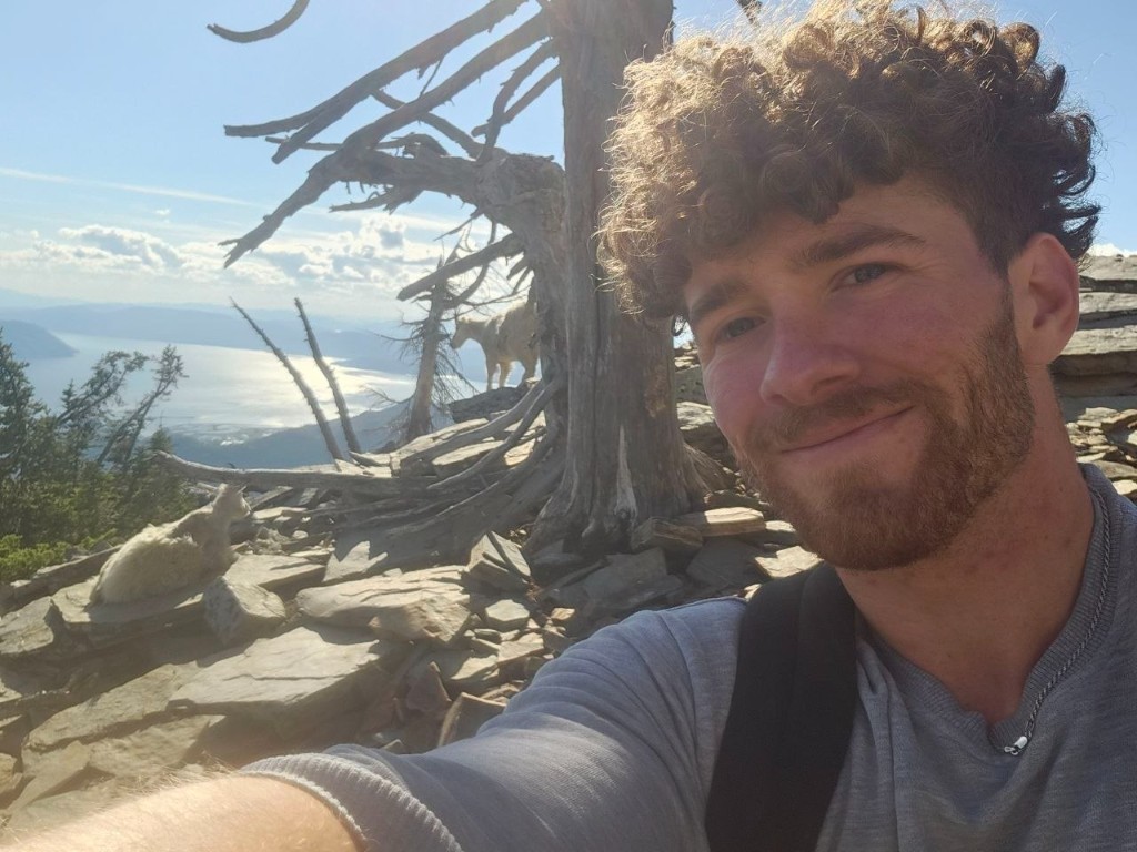 Brandon Moreau on a mountain hike with mountain goats in the background